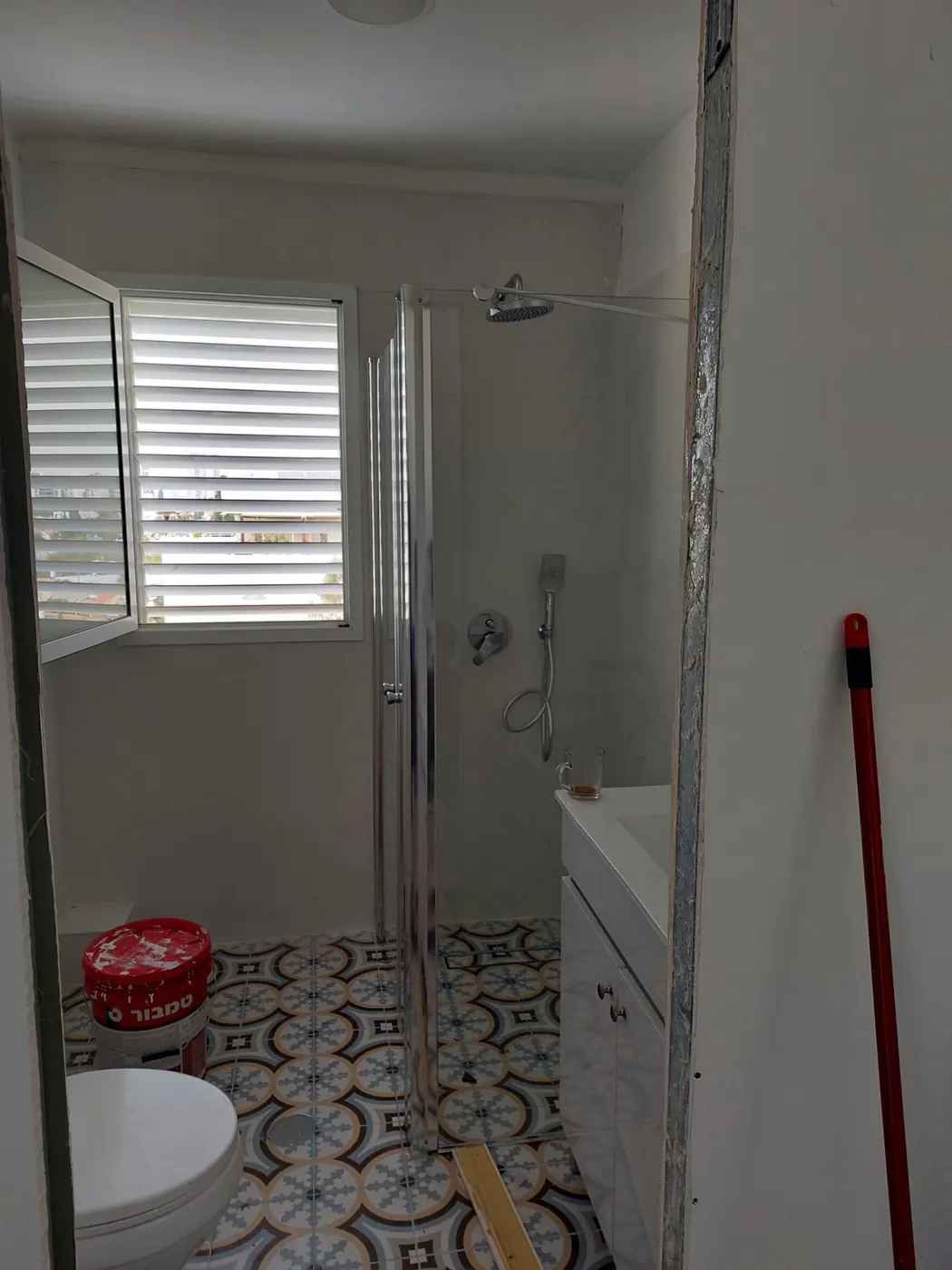 Une salle d'eau rénovée avec paroi de douche en verre et carrelage à motifs, juste avant la fin des travaux